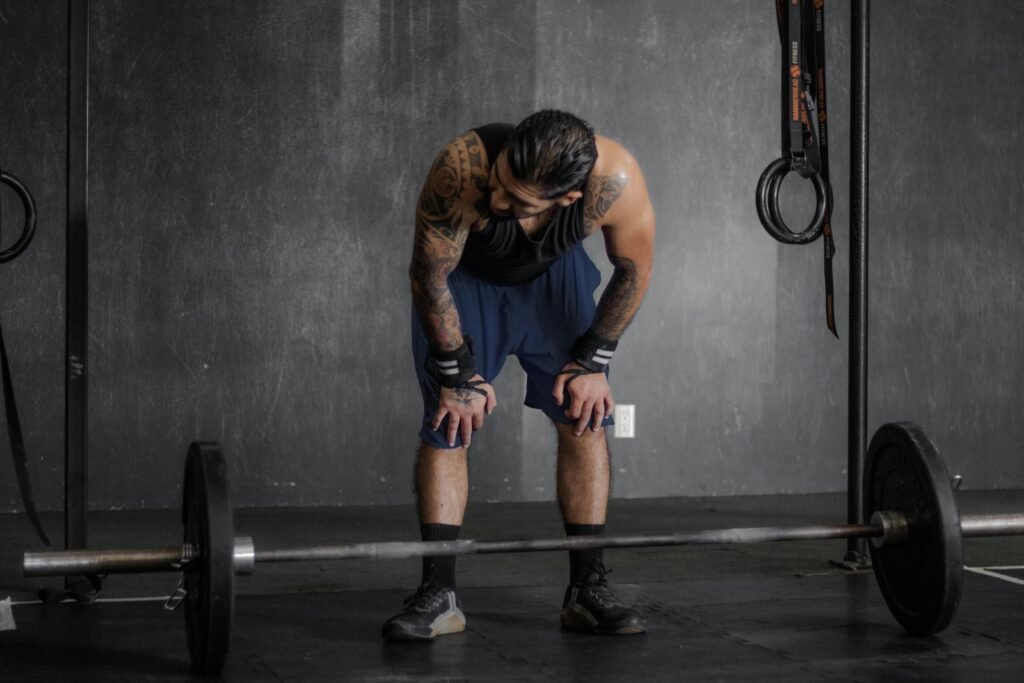 A muscular man with tattoos rests after an intense weightlifting session in the gym.