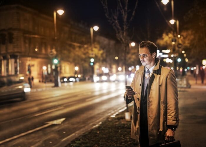 Man in formal wear reading phone on a city street at night.