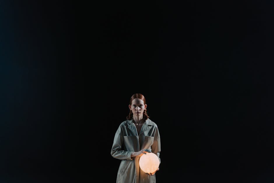 A redhead woman holding an illuminated sphere against a black background, evoking mystery.