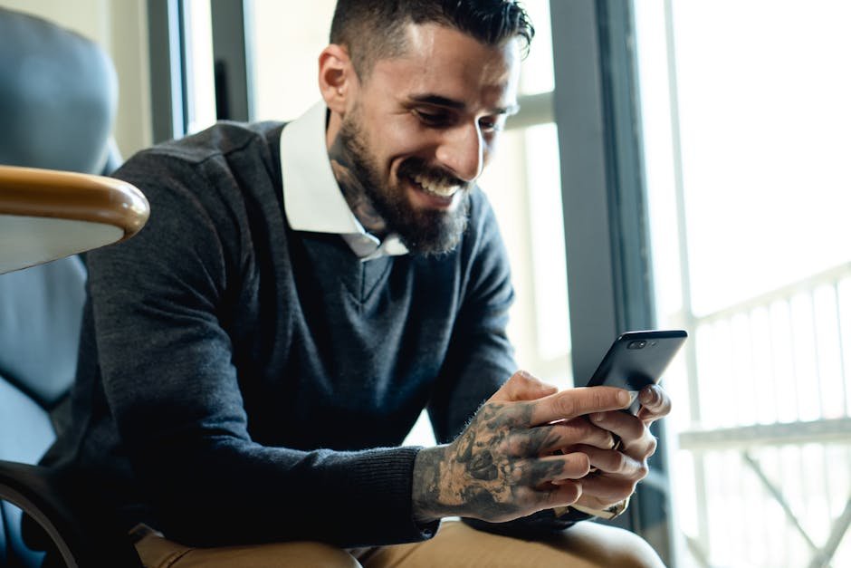 Happy bearded man in sweater checking his smartphone indoors, smiling