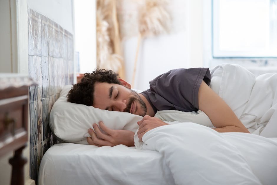 Man resting peacefully in bed, wrapped in white sheets, creating a serene and cozy atmosphere.