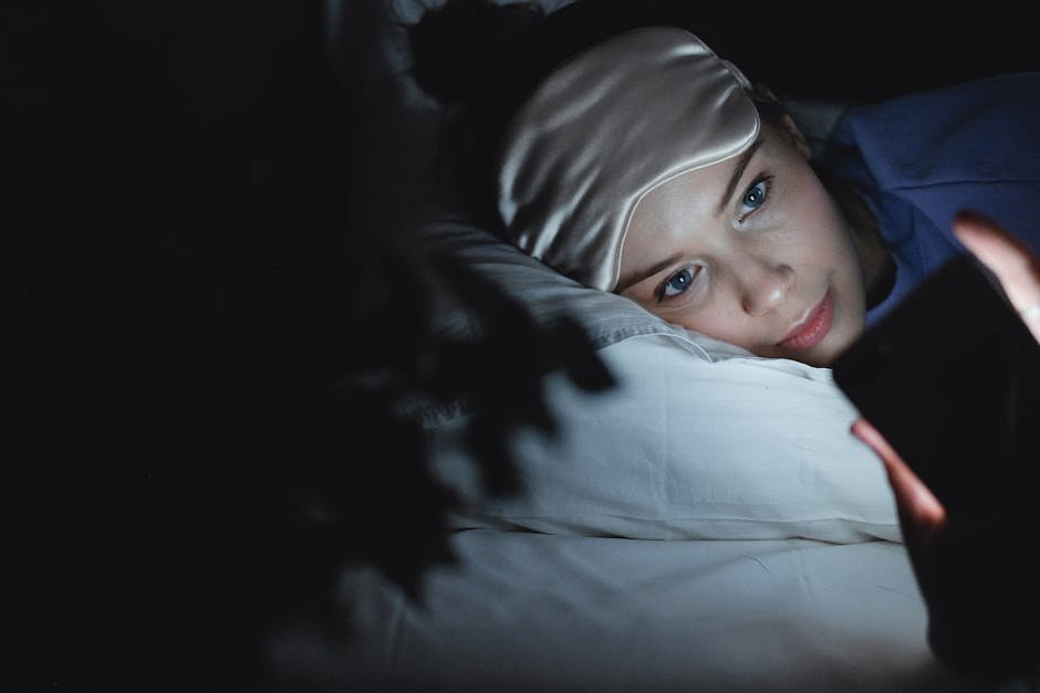 A woman in bed wearing a sleep mask uses her phone at night, creating a cozy ambiance.